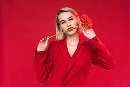 attractive girl with red gerbera flower in mouth, isolated on redの写真素材