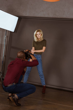 beautiful caucasian woman posing while african american photographer taking picture in studioの写真素材