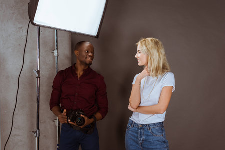 cheerful multiethnic photographer and model looking at each other while having photoshoot in studioの写真素材