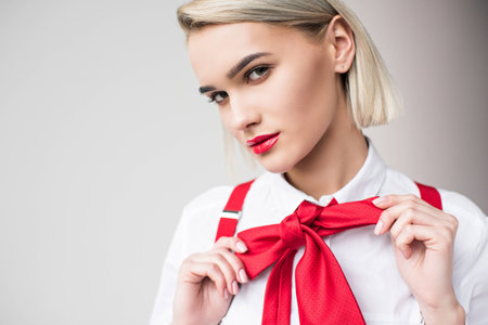 stylish girl posing in white shirt, red suspenders and bow, isolated on greyの写真素材