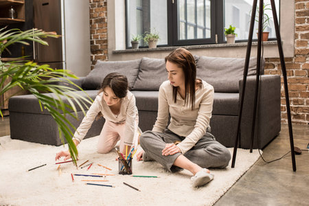 family sitting on floor and drawing picture together at homeの写真素材