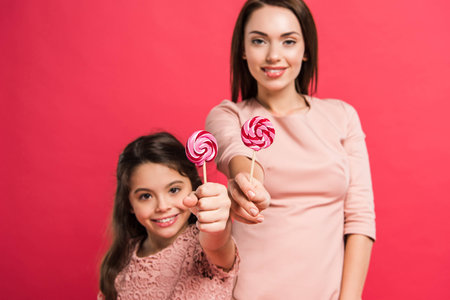 Mother and daughter showing lollipops isolated on redの写真素材