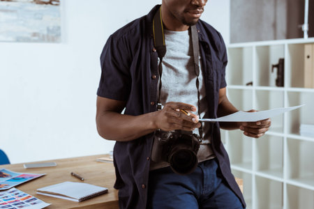 cropped shot of african american photographer with photoshoot examples in hands at workplaceの写真素材