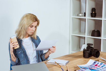 photographer with coffee to go looking at photoshoot samples at workplace in office