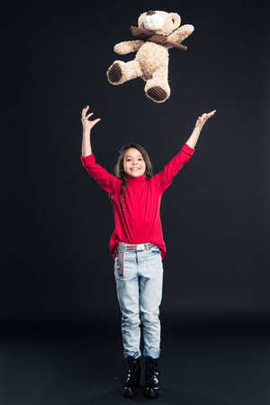 Happy kid throwing up teddy bear isolated on blackの写真素材