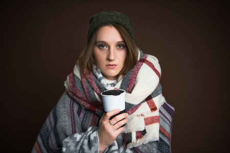 Girl in winter clothes holding thermal cup isolated on brownの写真素材