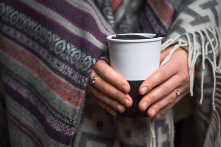 Cropped view of woman holding thermal cup in hands isolated on brownの写真素材
