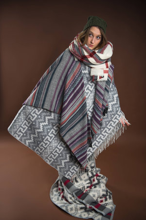 Girl standing wrapped in warm blankets isolated on brown