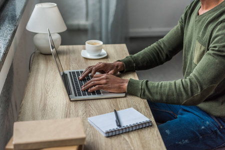 cropped shot of african american man typing on laptop while working at homeの写真素材