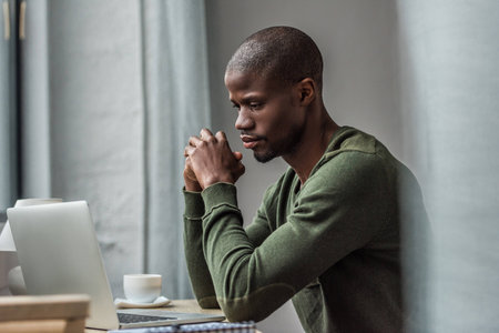 pensive african american man using laptop while working at homeの写真素材