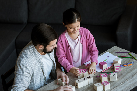 father with daughter sitting at table and making words by cubes with letters at homeの写真素材