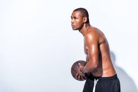 side view of shirtless african american man holding basketball ball and looking away on greyの写真素材