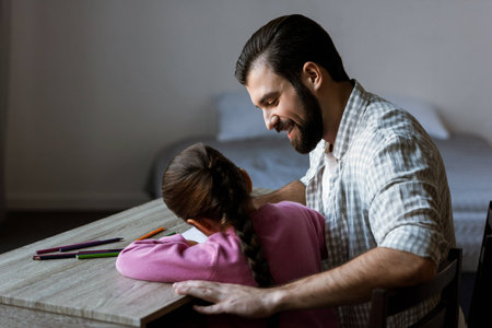 side view of father with little daughter sitting at table and drawing in scrapbook at homeの写真素材
