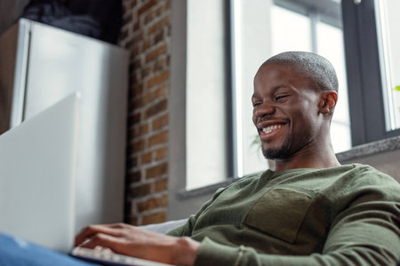 side view of cheerful african american man using laptop at homeの写真素材