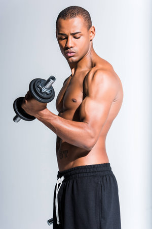 athletic young african american sportsman training with dumbbells isolated on grey