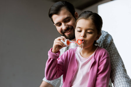 happy father with daughter blowing bubbles at homeの写真素材