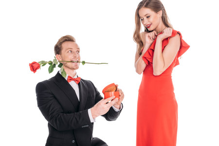 young man with rose flower in teeth proposing to woman isolated on whiteの写真素材