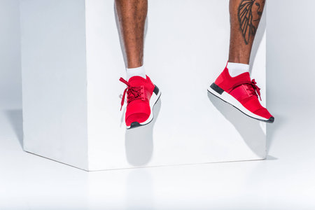 low section of african american man in red sneakers sitting on greyの写真素材