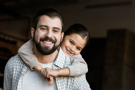 cheerful father and daughter hugging and looking at camera at homeの写真素材