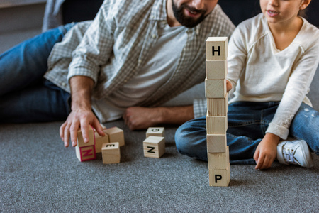 cropped image of father with daughter making words by cubes with letters at homeの写真素材