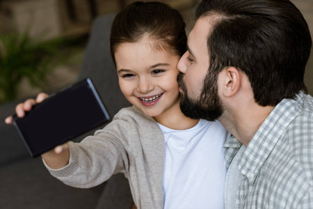 cheerful father with daughter taking selfie on smartphone at homeの写真素材