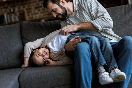 father with daughter laying on couch, hugging and laughing at homeの写真素材