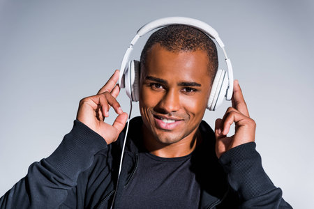 handsome young african american sportsman listening music in headphones and smiling at camera isolated on greyの写真素材