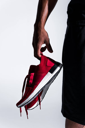 close-up partial view of african american sportsman holding sports shoes isolated on greyの写真素材