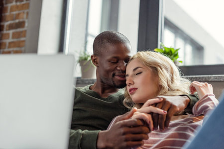 selective focus of sensual african american man hugging girlfriend while resting on sofa togetherの写真素材