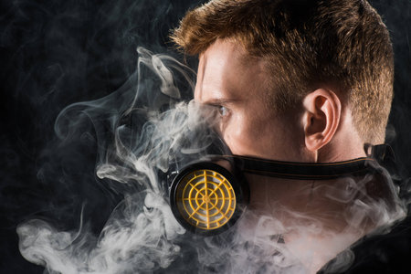 Man in black hood wearing protective filter mask surrounded by clouds of smoke