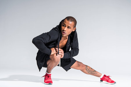 young african american man in sportswear stretching and looking away on greyの写真素材
