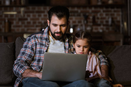 father with daughter sitting on couch and using laptopの写真素材