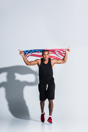 young african american sportsman holding american flag and running on greyの写真素材