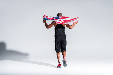 back view of young african american sportsman holding american flag on greyの写真素材