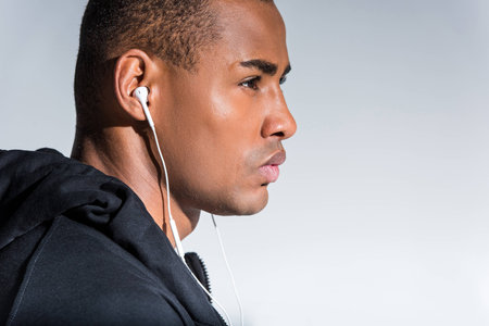 profile portrait of young african american man listening music in earphones and looking away  isolated on greyの写真素材
