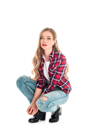 upset girl in checkered shirt and jeans crouching and looking at camera isolated on whiteの写真素材