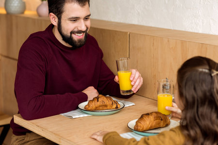 father and daughter drinking orange juice in cafeの写真素材