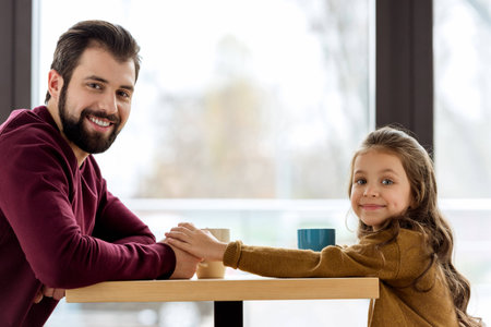 smiling father and daughter sitting in cafe and holding handsの写真素材