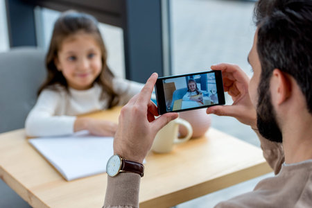cropped image of father taking photo of daughter in cafeの写真素材