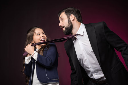 happy daughter pulling father tie on burgundyの写真素材