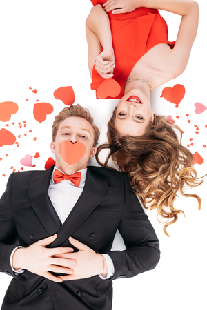 top view of young couple with red paper hearts smiling at camera and lying isolated on whiteの写真素材