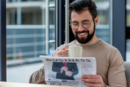 smiling man drinking coffee with marshmallow and reading business newspaperの写真素材
