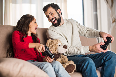 happy father and daughter playing video game at home and looking at each otherの写真素材