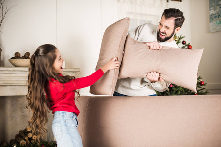 father and daughter beating with sofa pillows at homeの写真素材