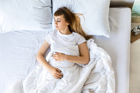 overhead view of young woman sleeping in bed in morningの写真素材