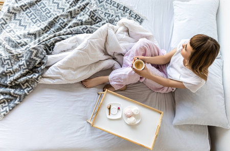 overhead view of woman with cup of coffee sitting on bed in morningの写真素材