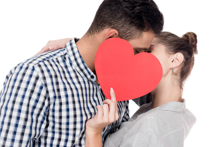 couple kissing and covering faces with paper heart isolated on white, valentines day conceptの写真素材