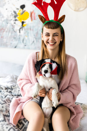 portrait of smiling woman with deer horns on head and puppy in santa hatの写真素材