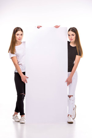young twins looking at camera while holding blank banner togetherの写真素材