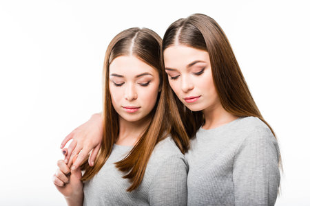 portrait of attractive twin sisters looking down isolated on whiteの写真素材